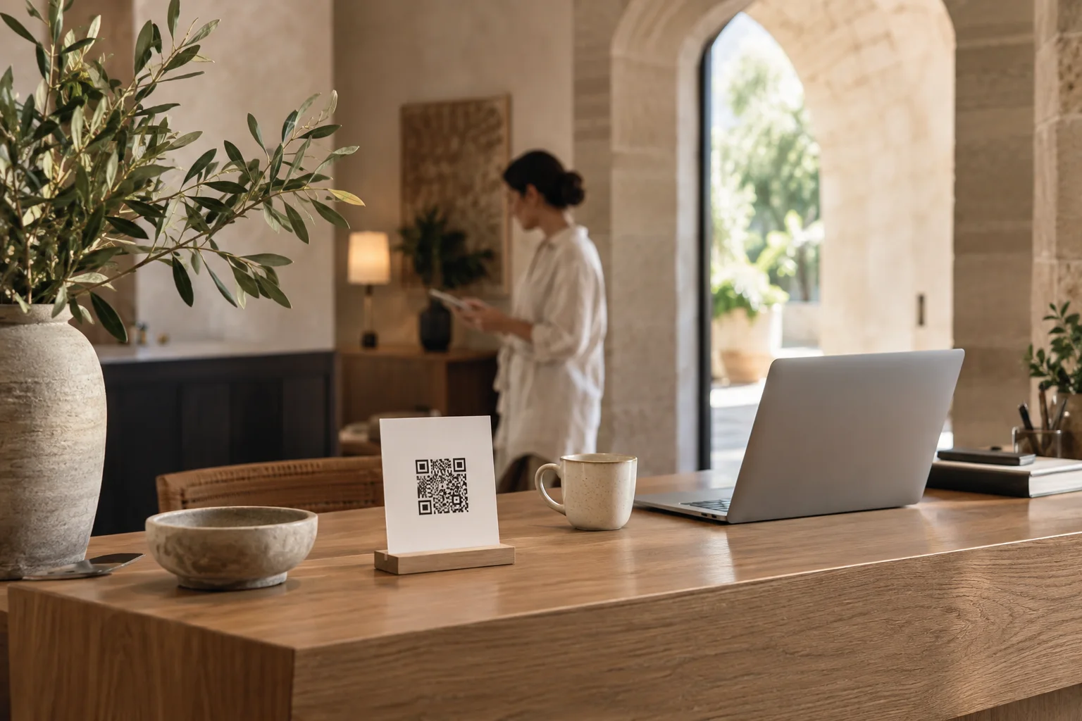 A laptop and printed QR code on a warm wooden reception desk in a boutique hotel.
